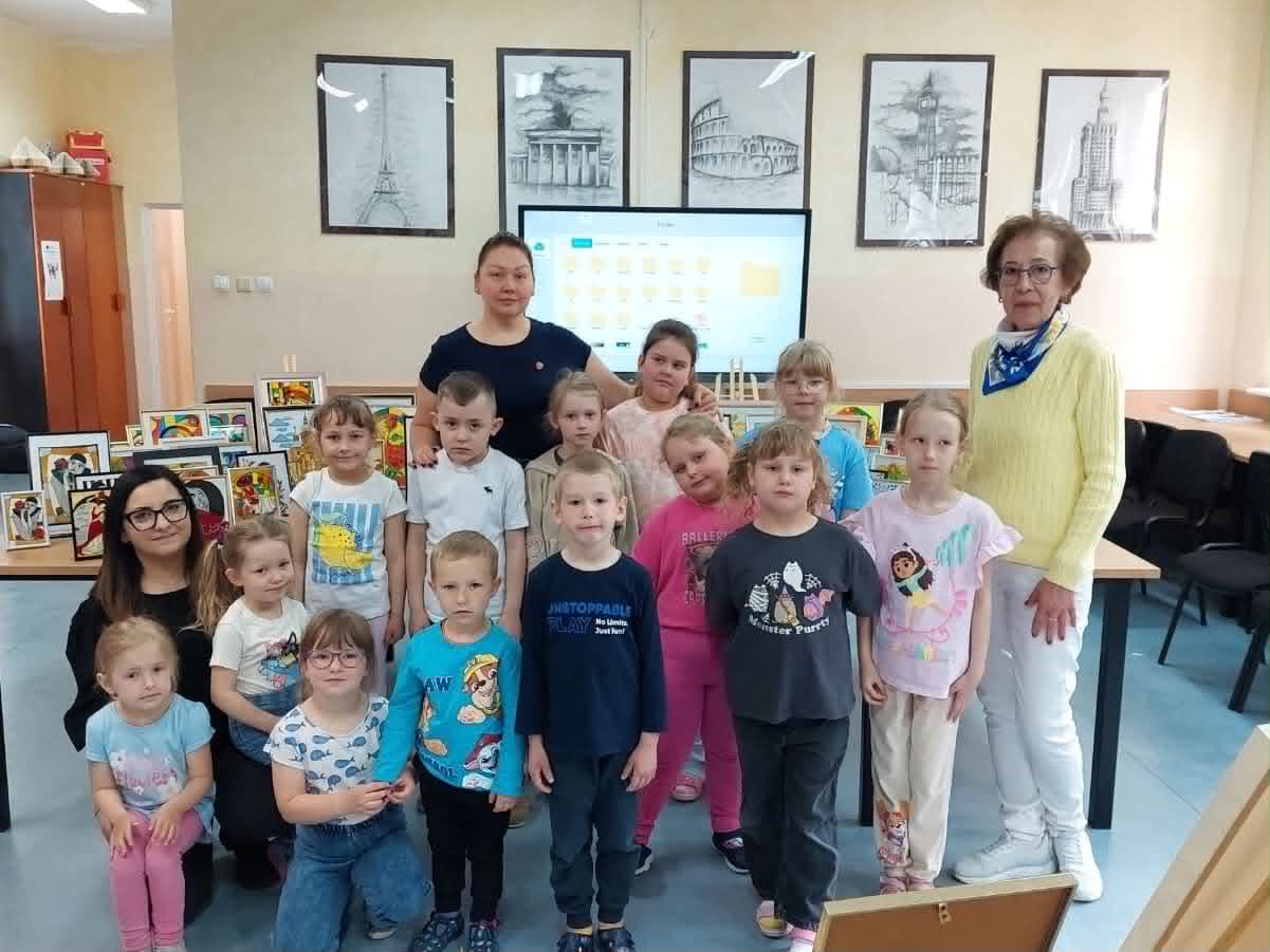Dzieci w wieku przedszkolnym pozują do zdjęcia z autorką prac, wychowawczynią i bibliotekarką.