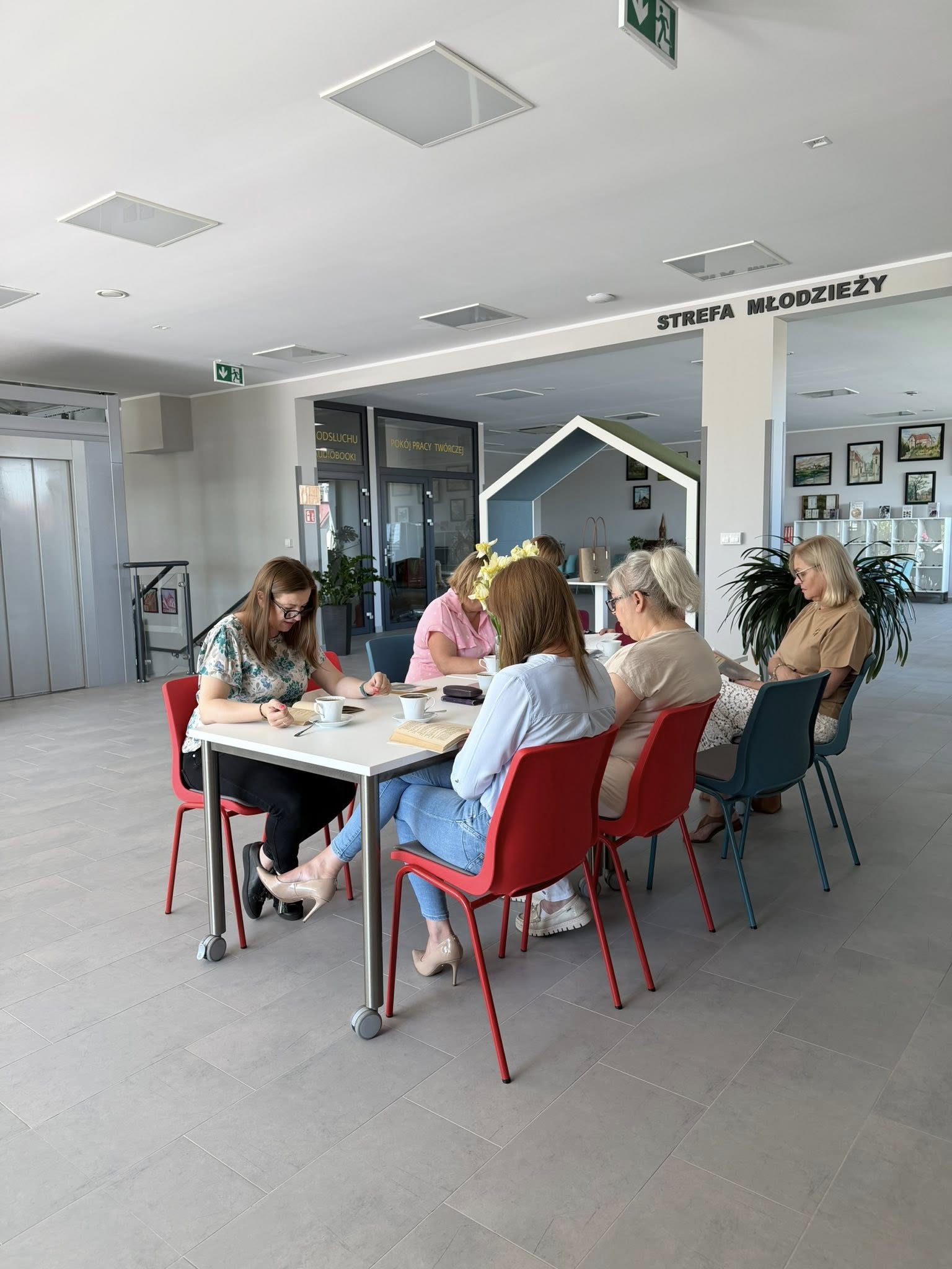 Uczestniczki spotkania siedzą zgromadzone wokół stołu, na stole książki i filiżanki z kawą.