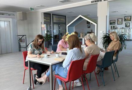 Uczestniczki spotkania siedzą zgromadzone wokół stołu, na stole książki i filiżanki z kawą.