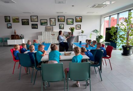 Bibliotekarka czyta książkę. Przedszkolaki siedzą przy stole.