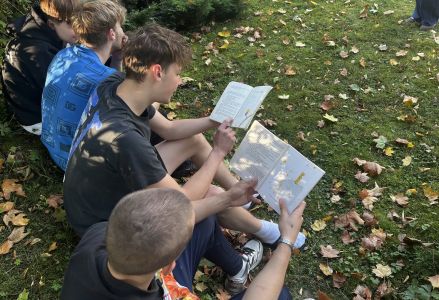 Uczniowie siedzą na trawie i czytają książki.
