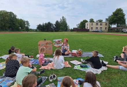 Bibliotekarka przebrana za Pippi pokazuje uczniom obrazek z wizerunkiem Pippi. Wszyscy siedzą na kocach.