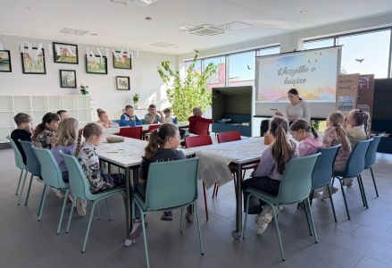 Drugoklasiści siedzący wokół stołu wysłuchują czytanego przez bibliotekarkę opowiadania.